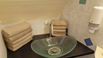 A bathroom with a glass sink, stacked towels, a soap dispenser, and a towel rack.