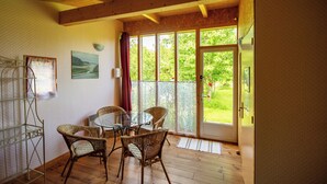 A room with a glass table, wicker chairs, a wooden ceiling, and a door leading to a garden. - Hôtel Rose (Beauvoir)