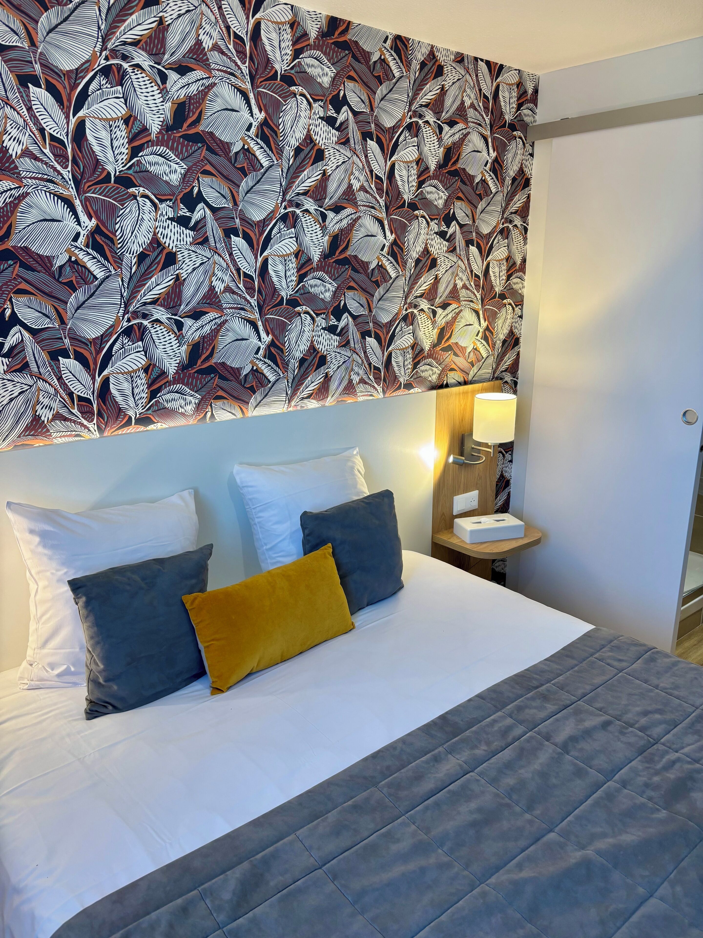 A neatly made bed with white and gray bedding, a mustard-colored pillow, and a gray quilt.