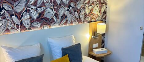 A neatly made bed with white and gray bedding, a mustard-colored pillow, and a gray quilt.