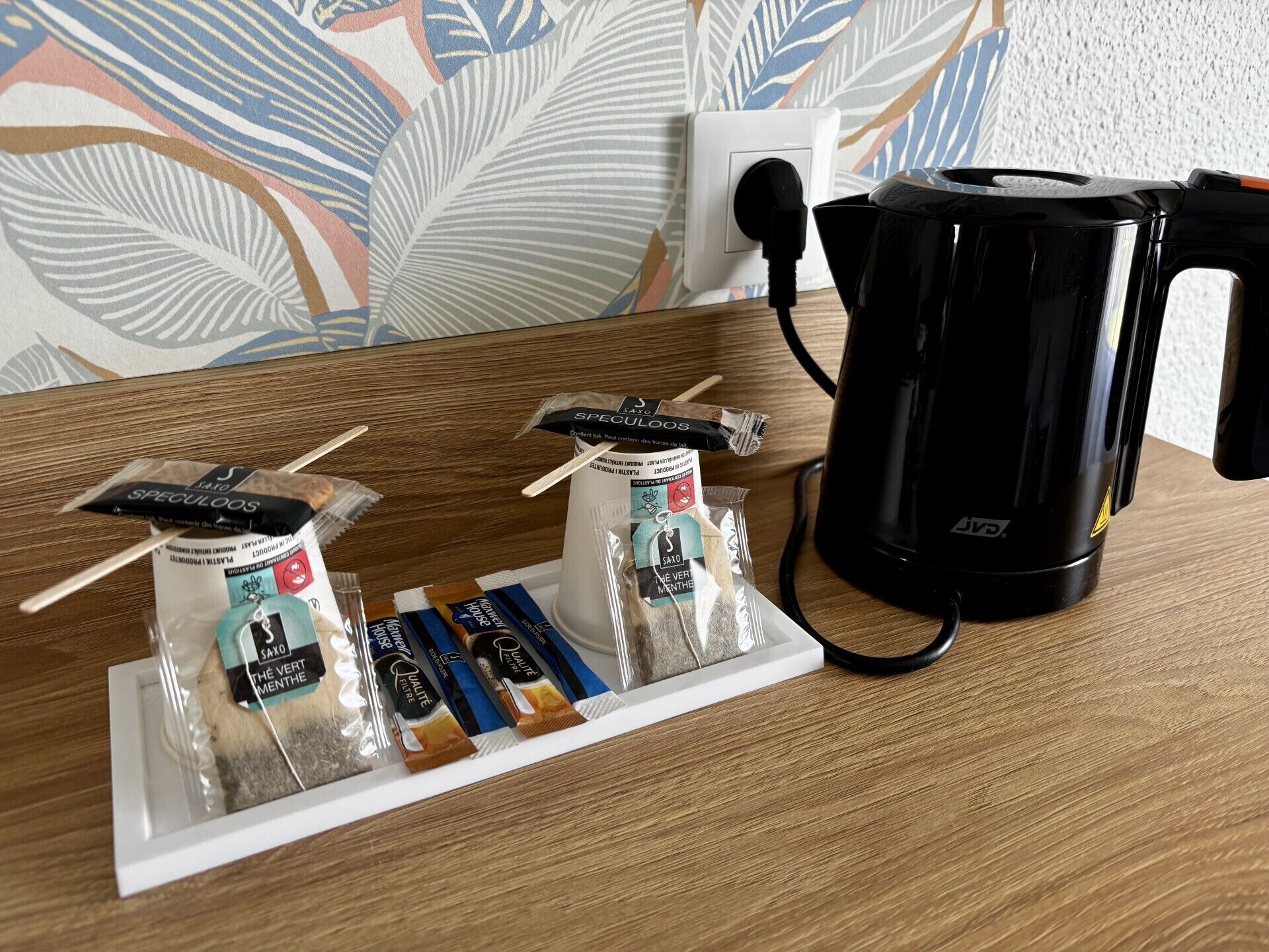 Eine Kaffeemaschine, ein weißes Tablett mit Kaffeekapseln und eine Wand mit Blättermotiv.