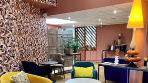 Un área de estar moderna con una pared decorada, un sillón amarillo, un sofá azul, una mesa redonda y una lámpara.