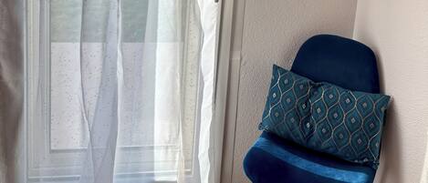A room with a sliding glass door, a blue chair with a patterned cushion, a wooden shelf, and a hanging wooden hanger.