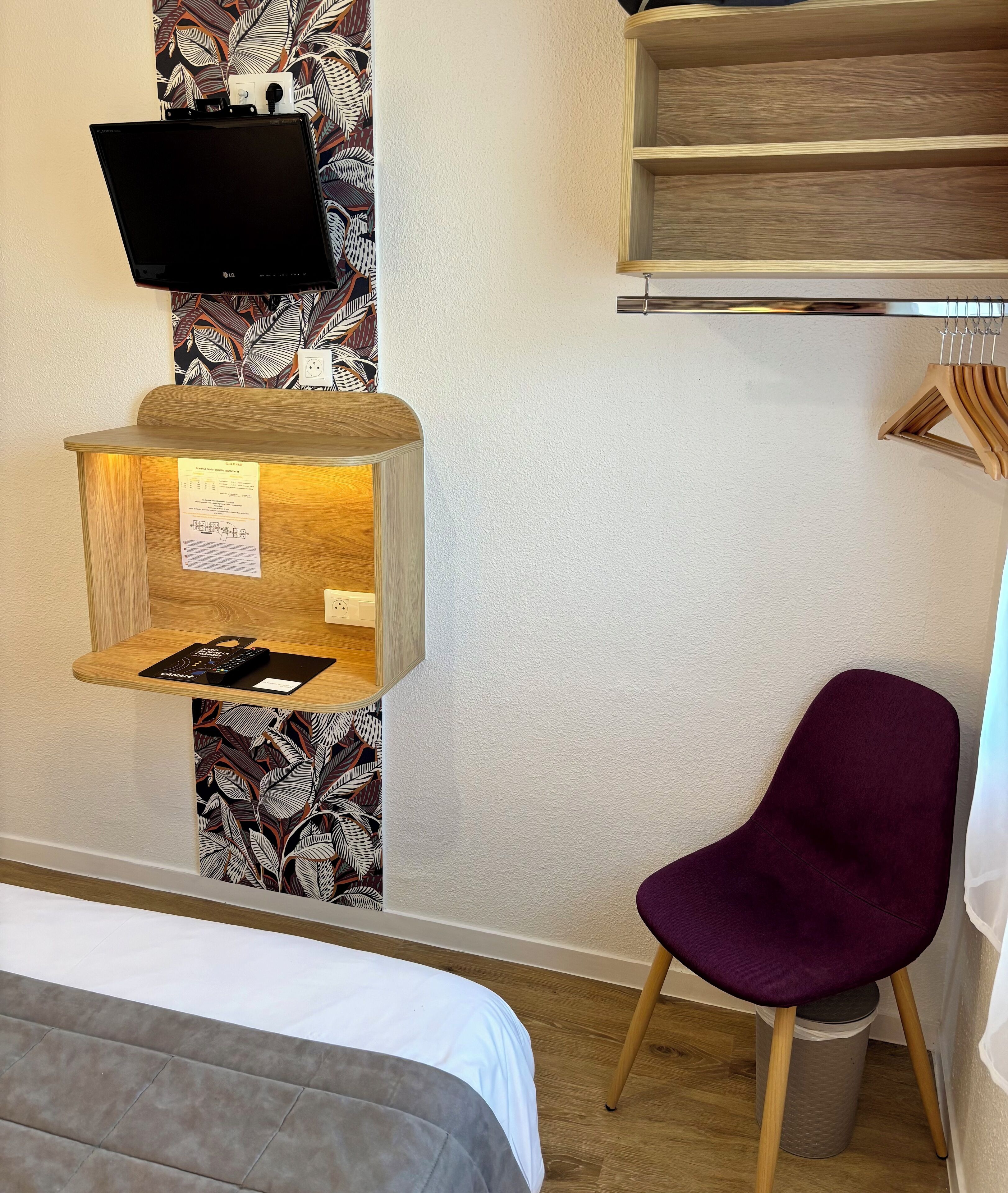 Habitación de hotel con cama, escritorio con monitor, una silla y televisor montado en la pared.