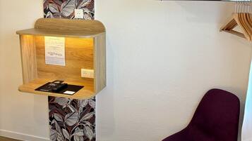 Habitación de hotel con cama, escritorio con monitor, una silla y televisor montado en la pared.
