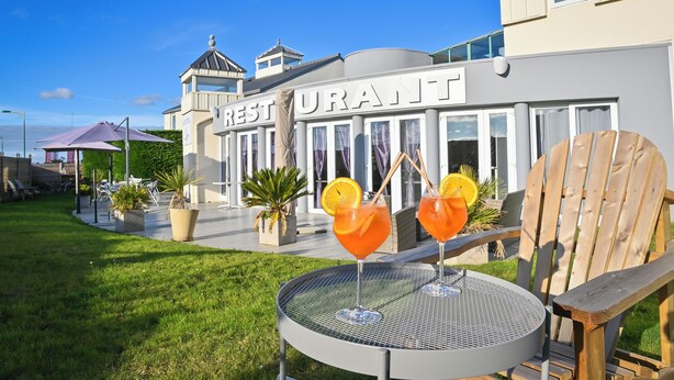 Restaurante con mesas al aire libre, una mesa redonda de metal y dos bebidas con rodajas de naranja.