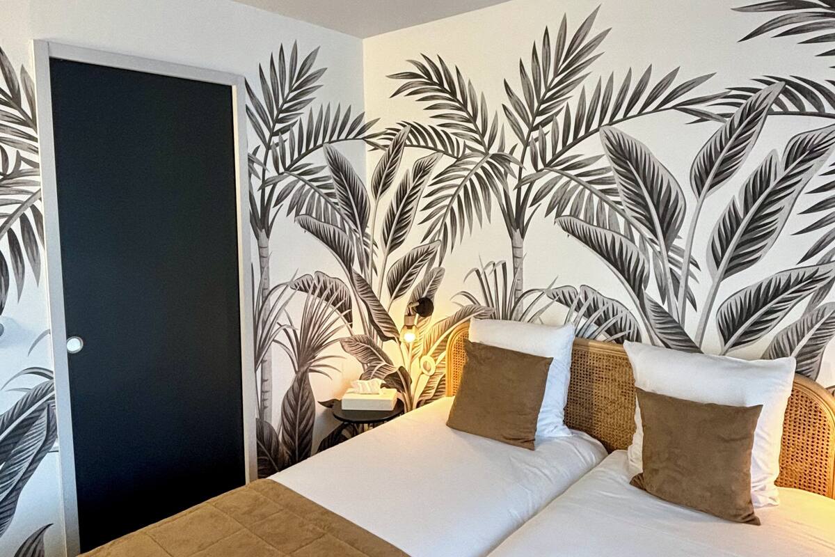A bedroom with a bed, pillows, and a wall mural of tropical leaves.
