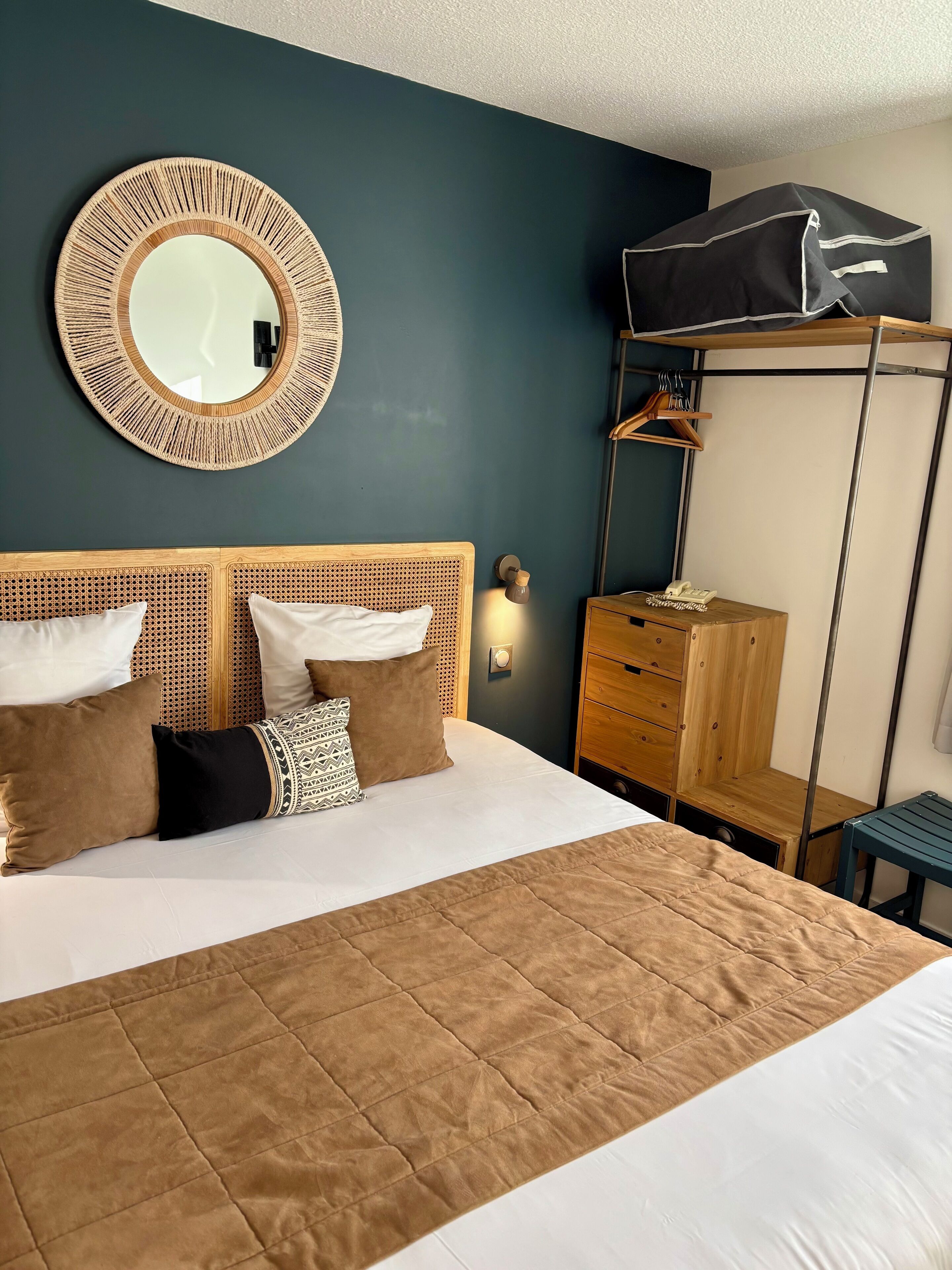 Une chambre d’hôtel bien aménagée, avec un grand lit, un miroir rond, une armoire et un porte-vêtements.