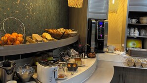 Un bufé de desayuno con diversos alimentos, una máquina de café y un refrigerador.