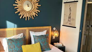 Une chambre à coucher avec un lit, une couvre-lit à motifs, un miroir décoratif fixé au mur et un tableau encadré représentant la Statue de la Liberté.