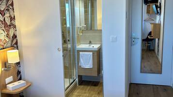 Habitación de hotel con cama, mesita de noche con lámpara, baño con lavamanos y espejo, y suelo de madera.