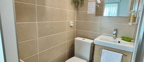 Un baño moderno con baldosas color beige, un inodoro blanco, un lavabo con un recipiente verde y un espejo.