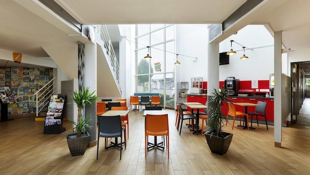 A modern cafe with wooden flooring, orange and black chairs, and a red counter. - hotelF1 Reims Tinqueux (Tinqueux)