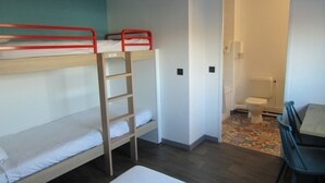 A dormitory room with bunk beds, a small table, and a chair. There is a bathroom with a toilet and a shower. - hotelF1 Reims Tinqueux (Tinqueux)