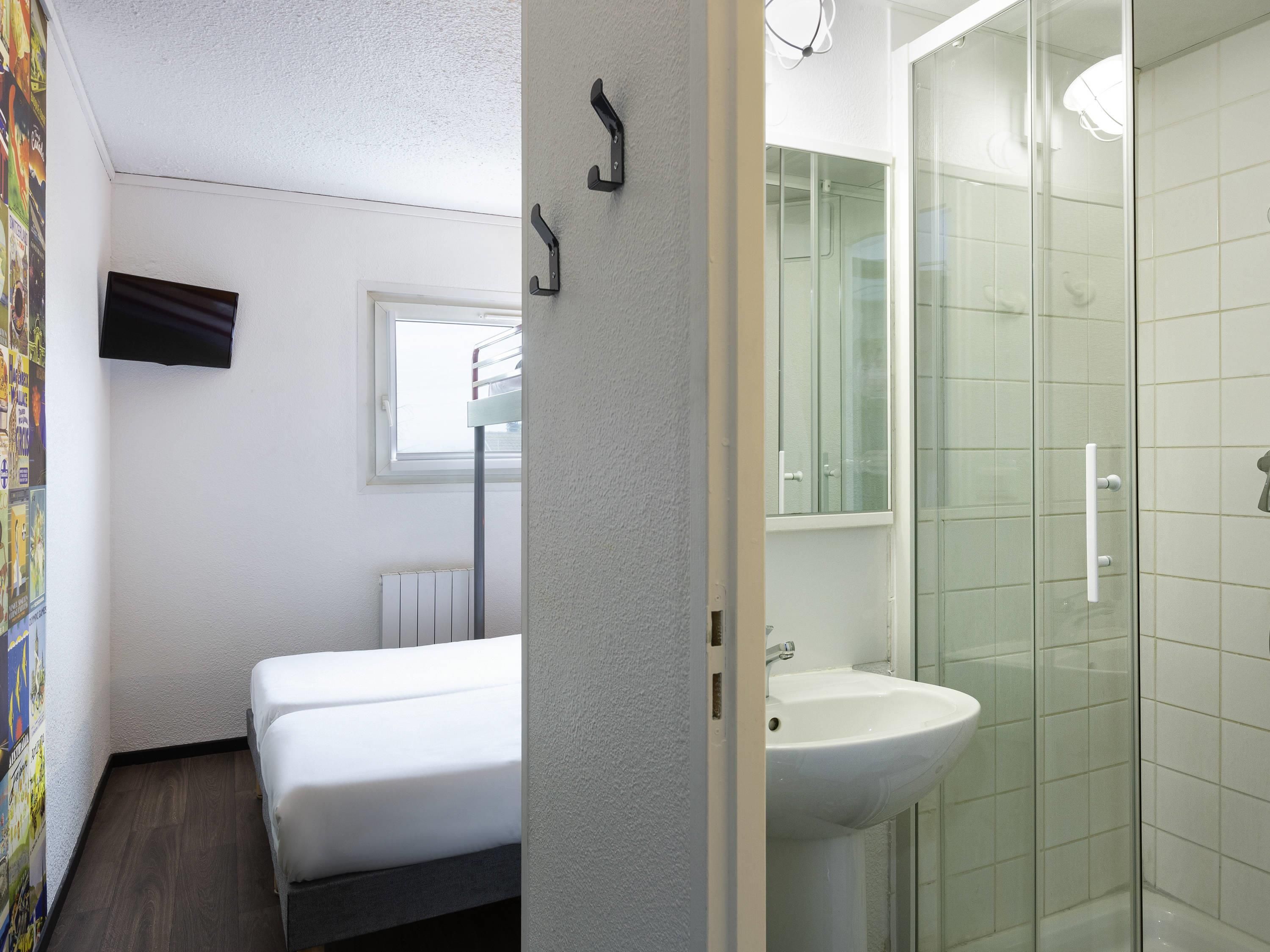 A hotel room with a bed, a window, a radiator, a sink, and a shower.