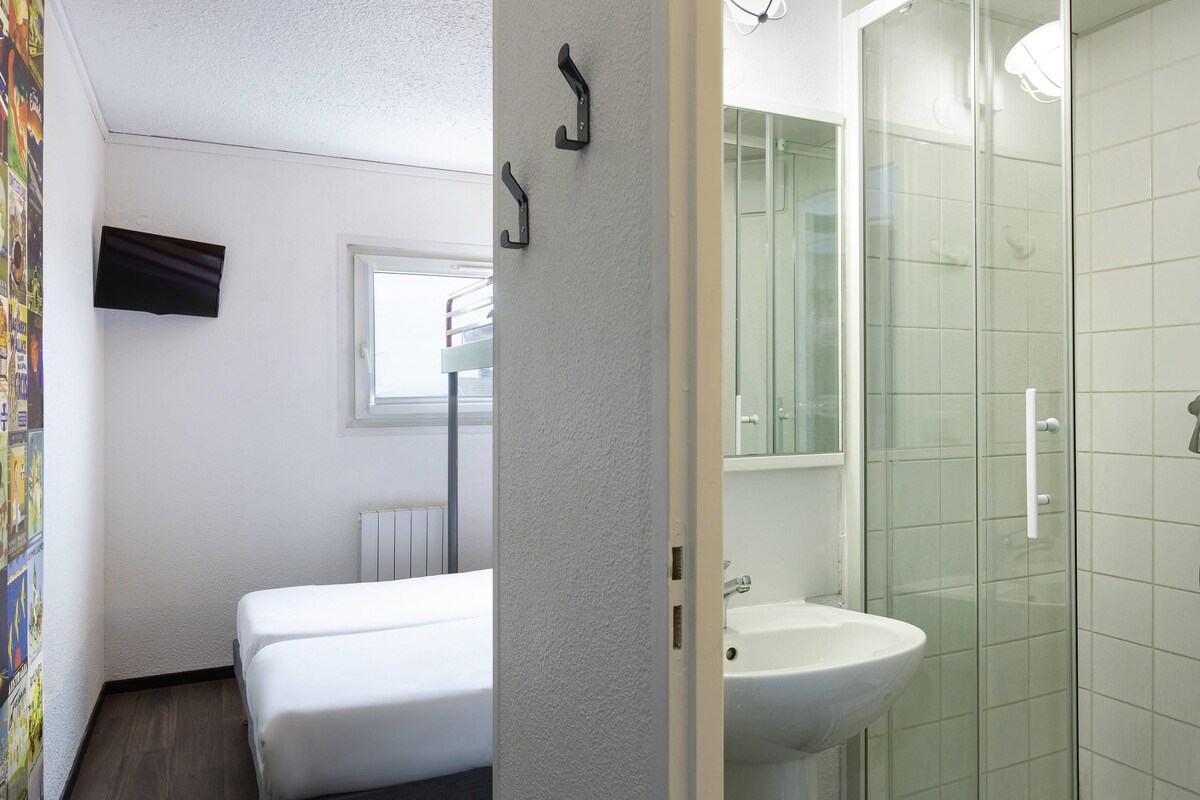 A hotel room with a bed, a window, a radiator, a sink, and a shower.