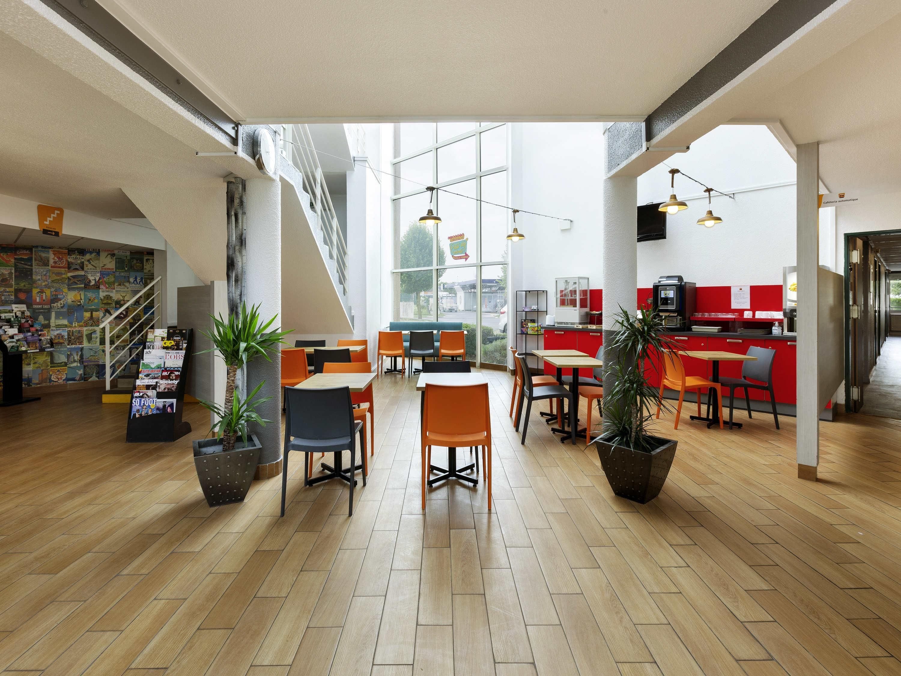 Una cafetería moderna con suelo de madera, sillas negras y anaranjadas, y una barra roja.