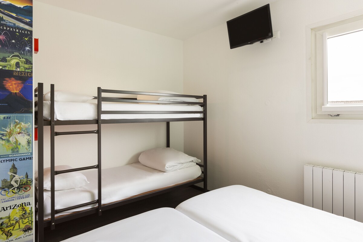 A bunk bed room with a white mattress, a wall-mounted TV, and a window with blinds.