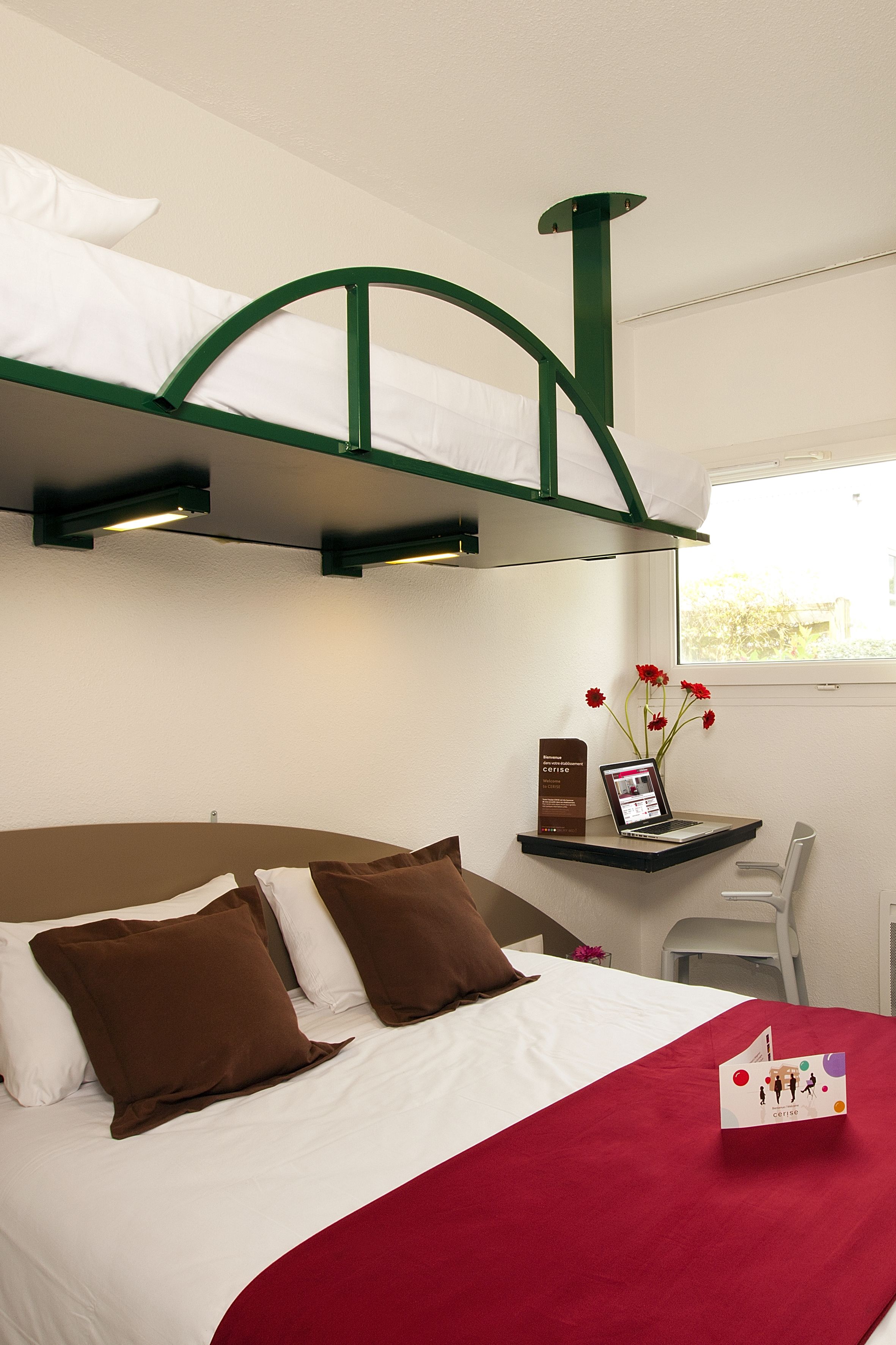 A bunk bed with a desk and chair, a laptop, and a vase with flowers.