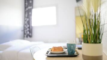 A breakfast tray with a pastry and a cup on a table, a potted plant, and a window with a view of a building.
