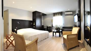 Une chambre d’hôtel avec un grand lit, deux fauteuils en osier, une petite table, un bureau, un canapé et un téléviseur.
