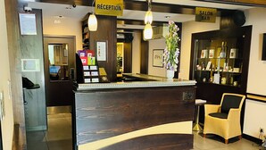 A reception desk with a wooden finish, a reception area, and a salon bar. - Cottage Hotel (Vandœuvre-lès-Nancy)
