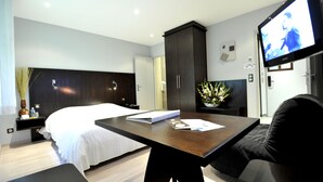 A modern hotel room with a large bed, a desk with a flat-screen TV, a dark wooden wardrobe, and a small plant on the desk. - Cottage Hotel (Vandœuvre-lès-Nancy)