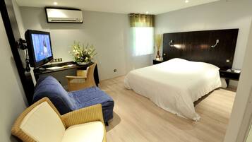Ein Hotelzimmer mit einem Bett, einem Schreibtisch mit Computer, einem Stuhl, einem kleinen Tisch mit einer Vase und einer Klimaanlage.