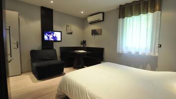 Una habitación de hotel con cama, escritorio, silla, televisor y aire acondicionado.