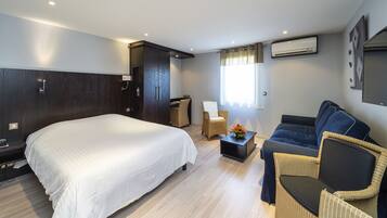 A hotel room with a large bed, a sofa, a chair, a desk, and an air conditioning unit.