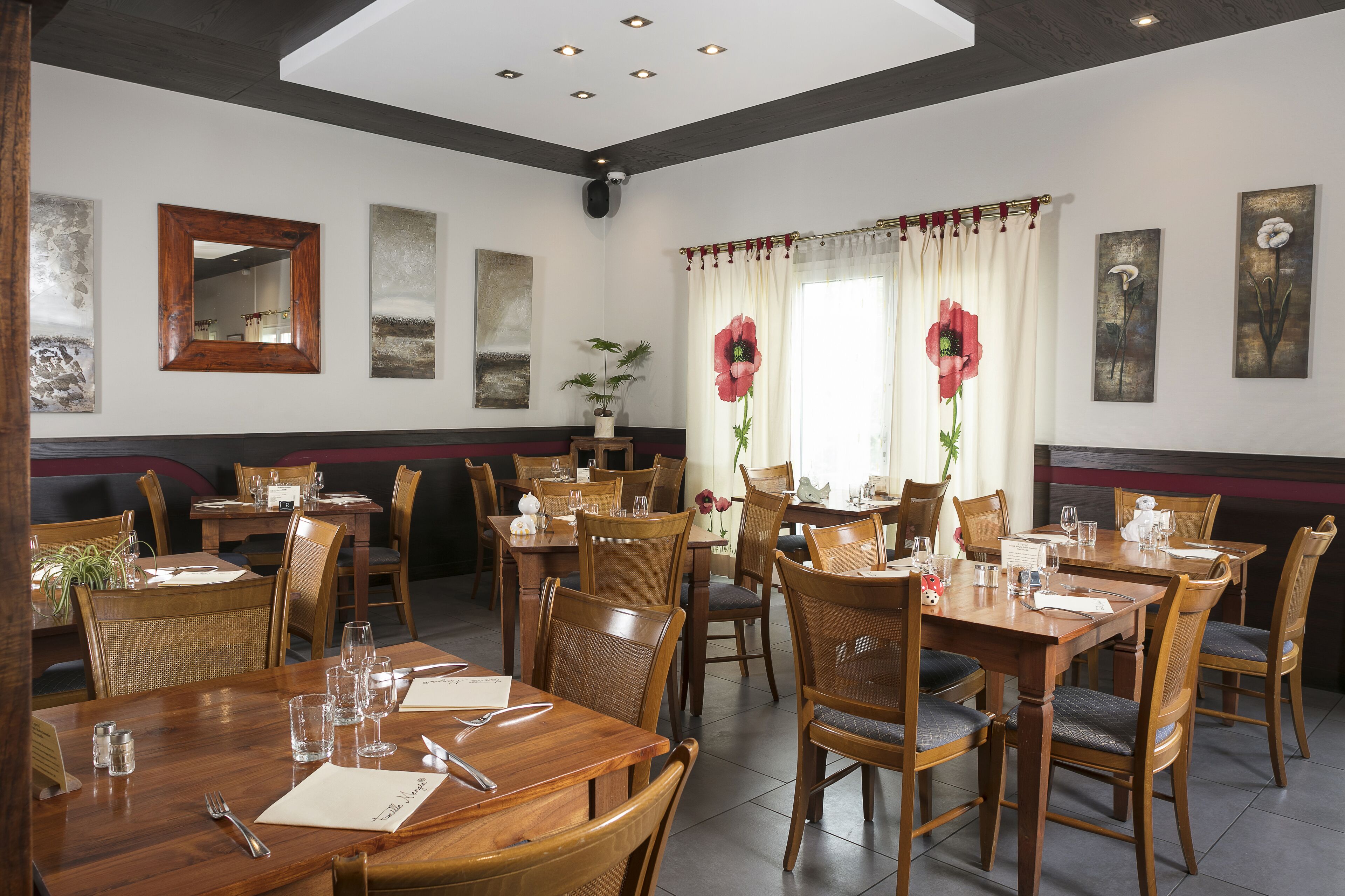 Un restaurante con mesas y sillas de madera, un espejo grande y obras de arte en las paredes.