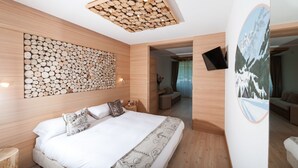 A modern bedroom with a wooden log wall, a large bed with patterned pillows, and a mounted TV. - Dahu (Pinzolo)
