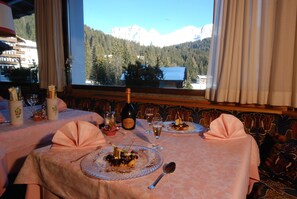 A dining table set with plates of food, wine glasses, and a bottle of wine, with a mountain view through a window. - Dahu (Pinzolo)