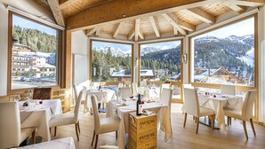 A restaurant with multiple tables, white chairs, and a wooden ceiling. Large windows offer mountain views. - Dahu (Pinzolo)