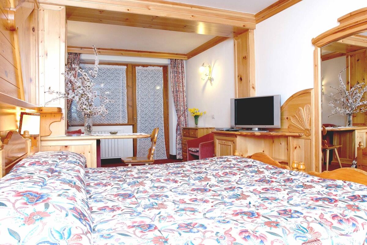 A wooden cabin interior with a bed, a desk, and a television.