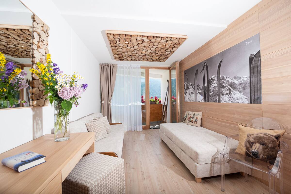 A modern room with a wooden ceiling, a sofa, a chair, a table with a book, and a vase with flowers.
