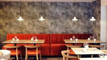 Un restaurant amb una banca vermella amb coixins, taules de fusta i lluminàries penjants.