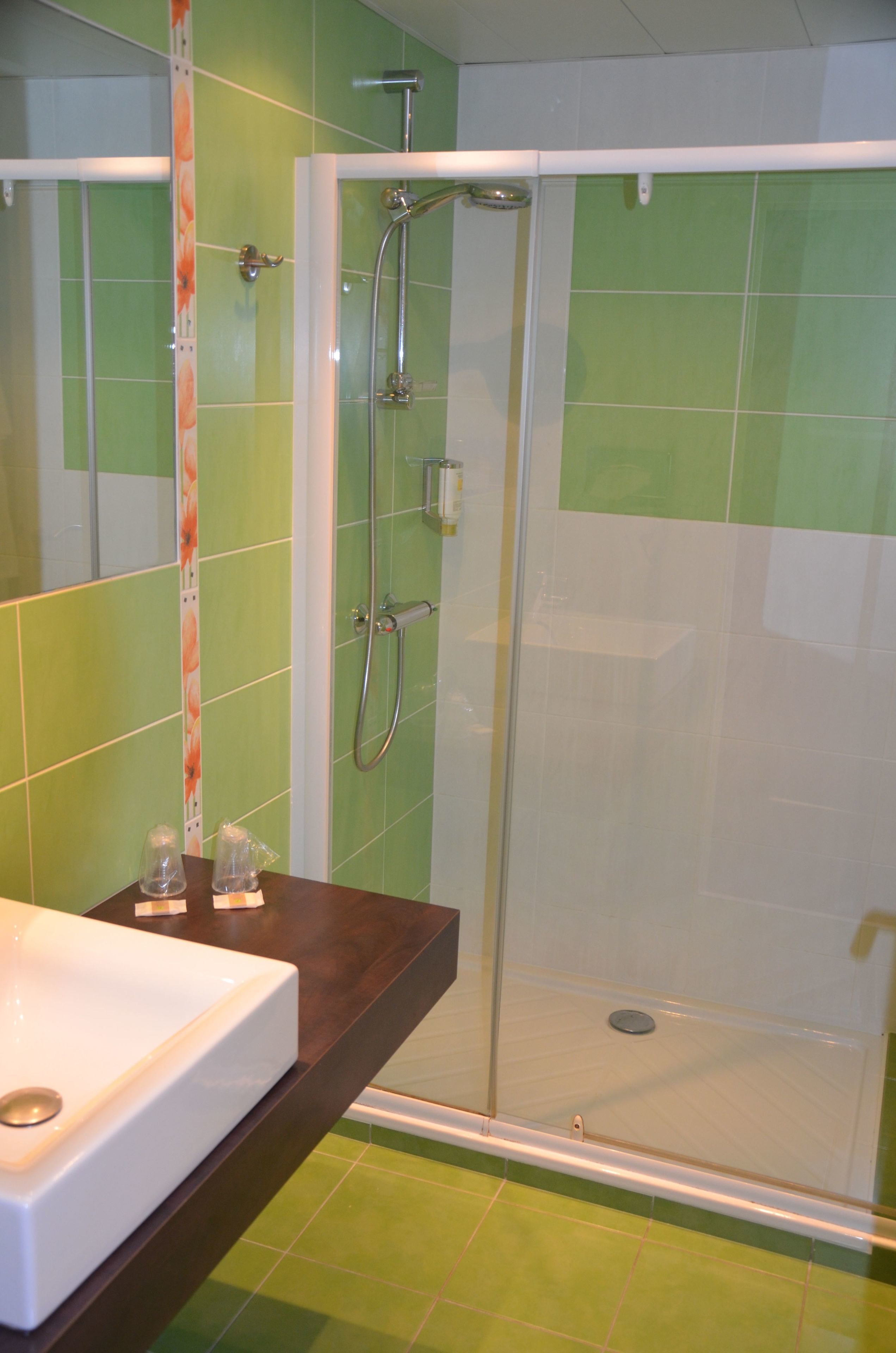 Une salle de bain avec une douche, un lavabo et des carreaux verts.