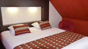 Habitación de hotel con una cama grande, dos almohadas, una manta de lunares, una silla roja y un cabecero con luces.