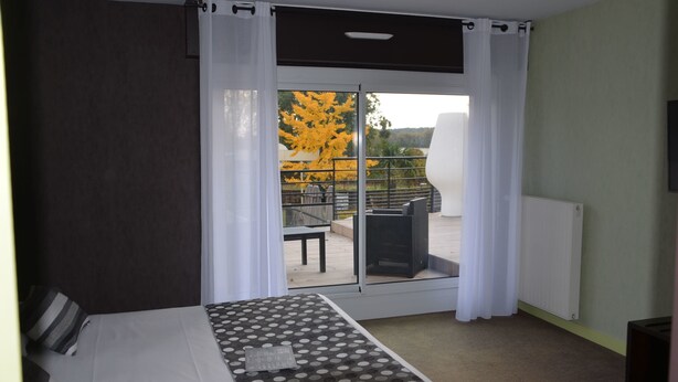 A bedroom with a bed, a window with curtains, a view of an outdoor patio with a table and chairs, and a radiator on the wall. - Golfe Hotel (Vannes)