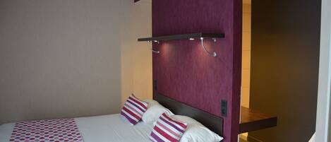 Habitación de hotel con una cama, almohadas, cabecero, estante y un baño visible al fondo.