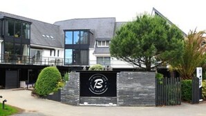 A modern building with a large logo on the facade, a covered entrance, and a well-maintained lawn. - Golfe Hotel (Vannes)