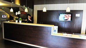 A reception desk with a dark wood finish, a flat-screen TV mounted on the wall, and a staircase in the background. - Golfe Hotel (Vannes)