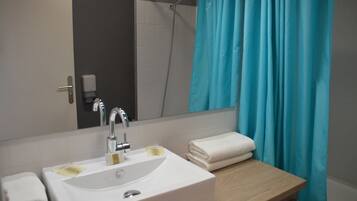 A bathroom with a white sink, a mirror, a shower, and a wooden vanity.