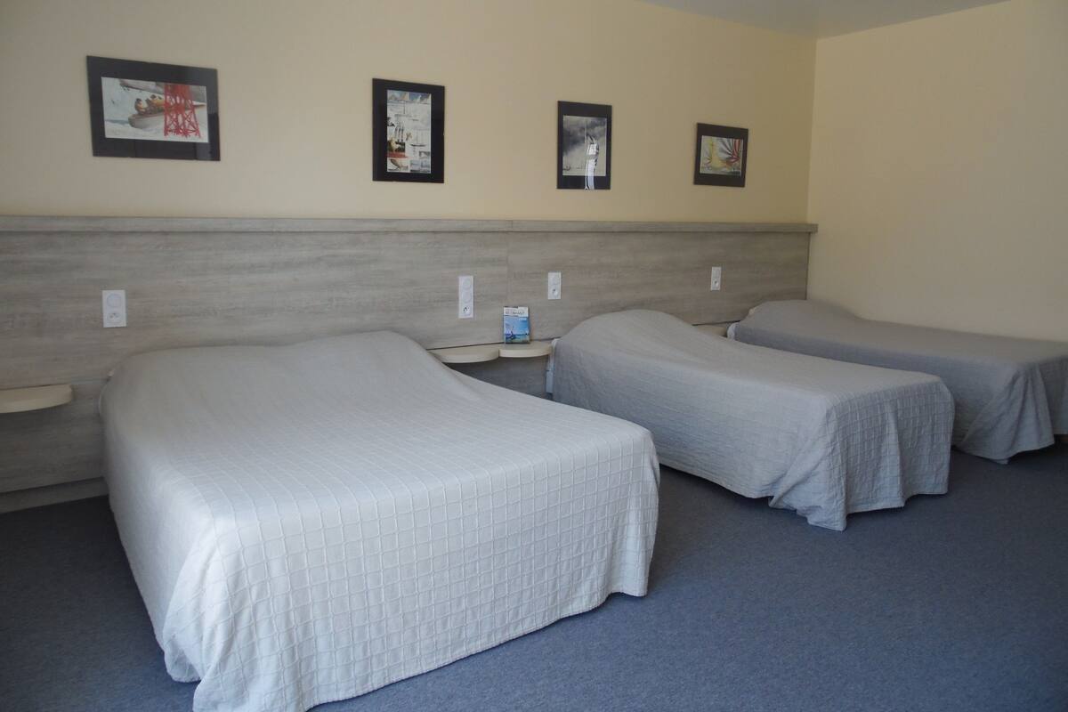 Une chambre d’hôtel avec deux lits simples, une tête de lit et quatre tableaux encadrés accrochés au mur.