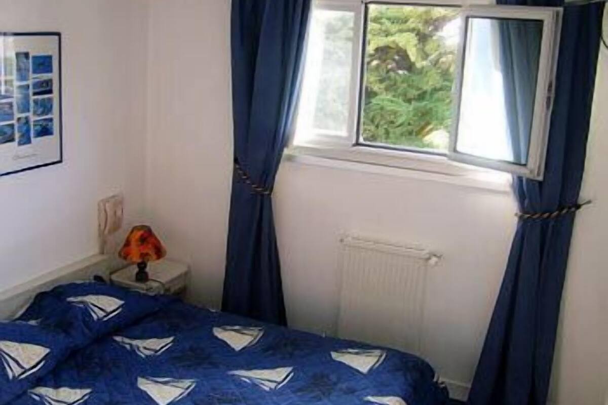 Une chambre à coucher avec un lit, une fenêtre avec des rideaux, un radiateur et une lampe sur une table de chevet.