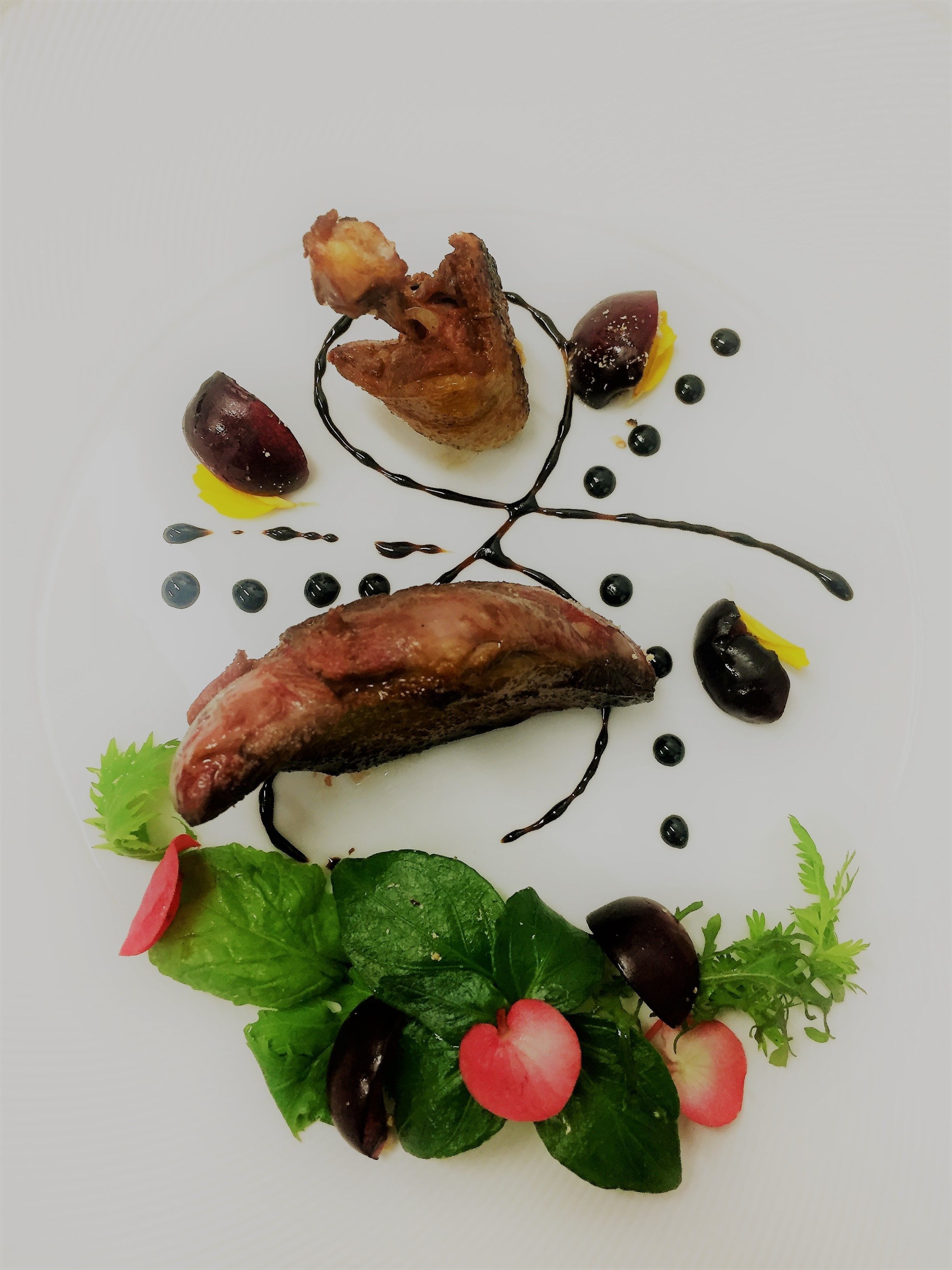 A white plate with a duck, olives, and a decorative sauce arrangement.