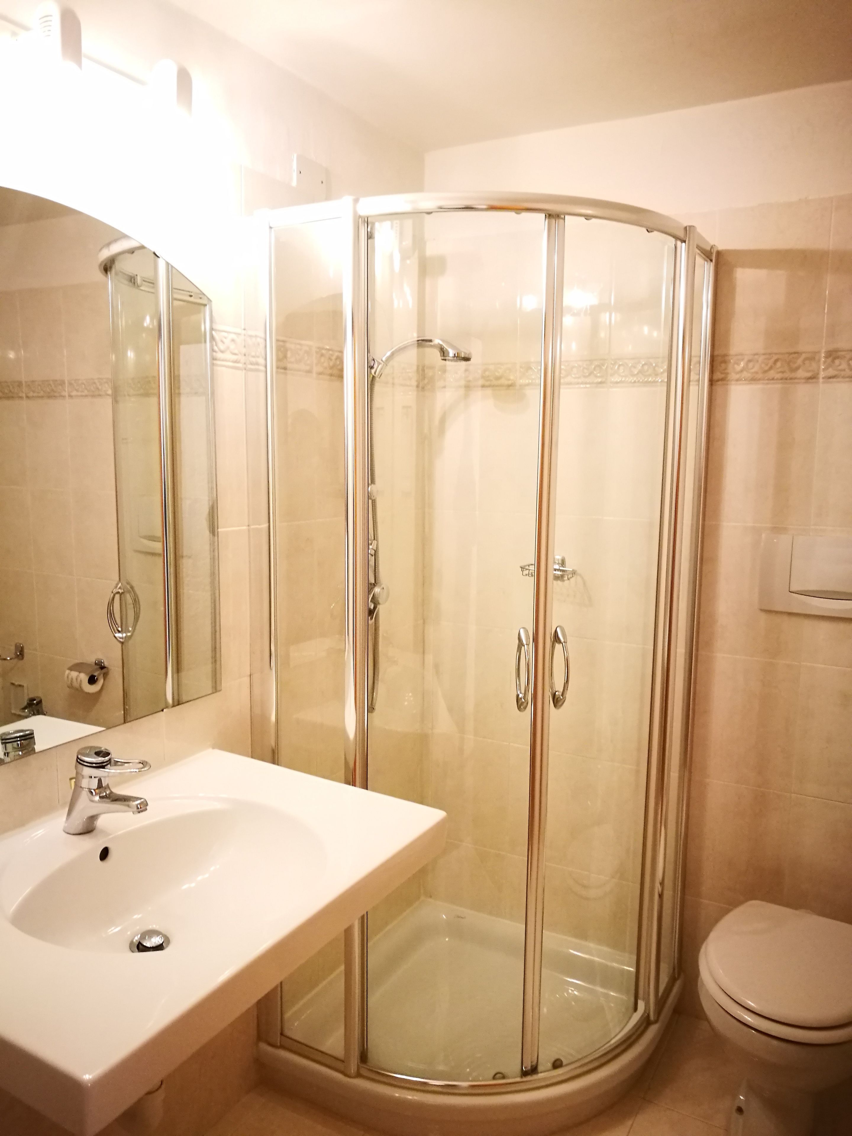 Een badkamer met een douchecabine van glas, een wastafel en een toilet.