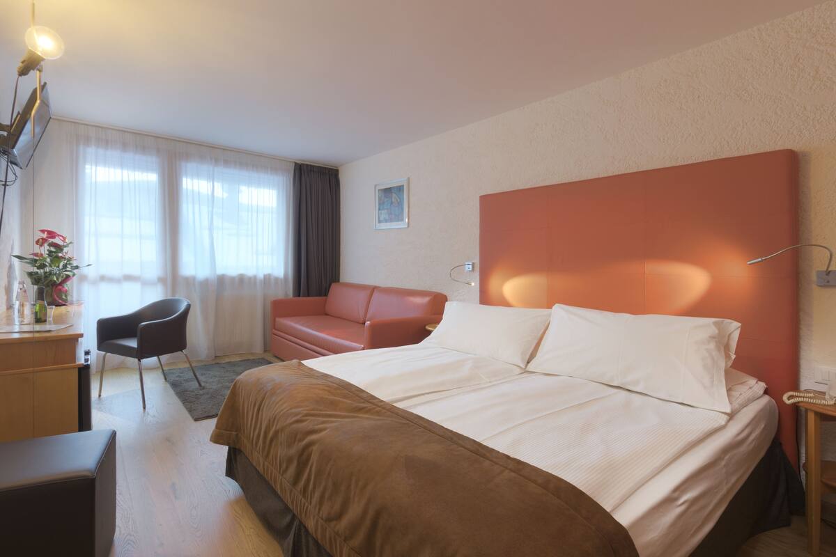 Una camera d'albergo con un letto grande, una scrivania con una sedia, un divano e un comodino con una lampada.