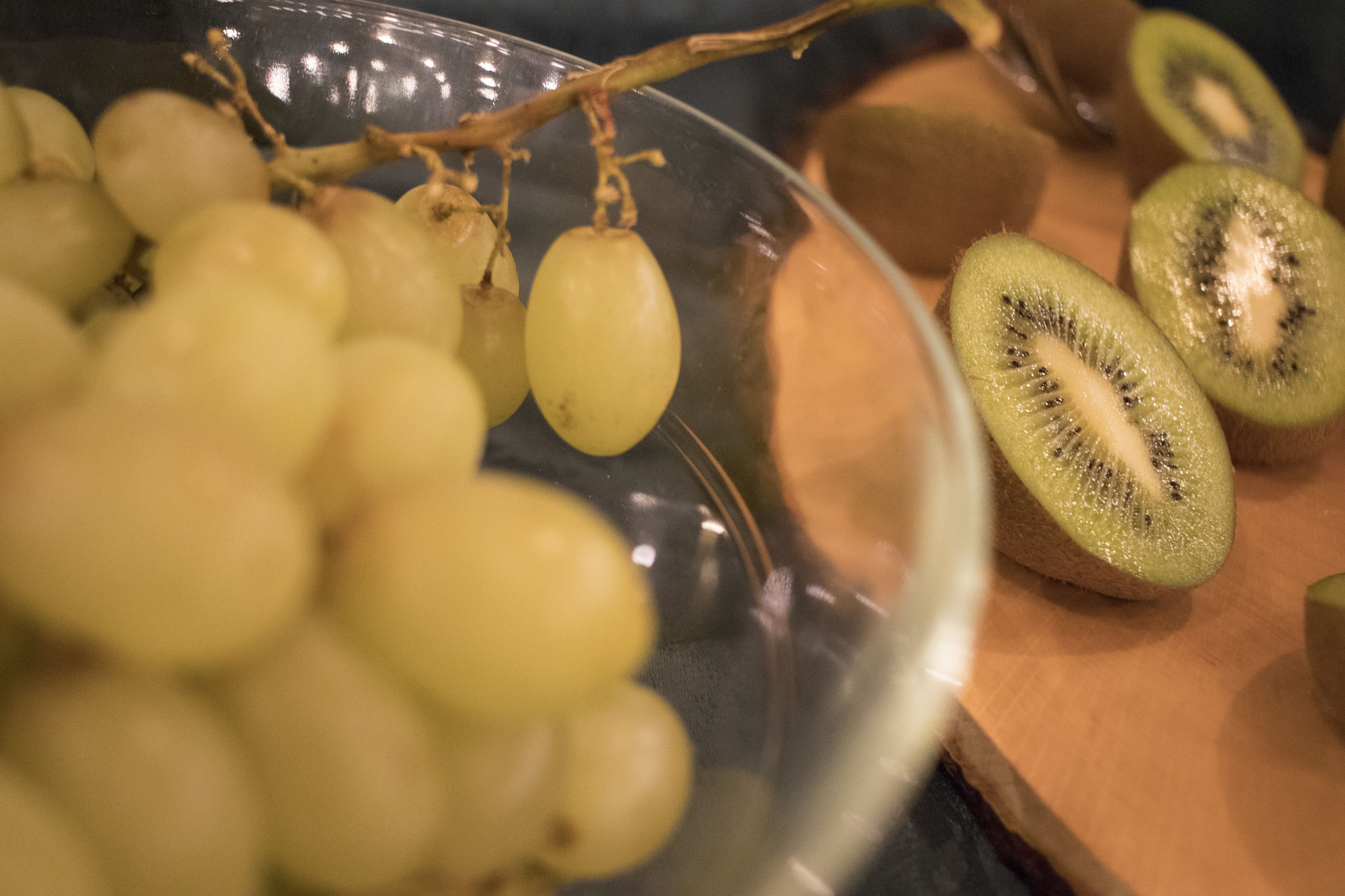 Un tazón de uvas verdes y medio kiwi sobre una superficie de madera.